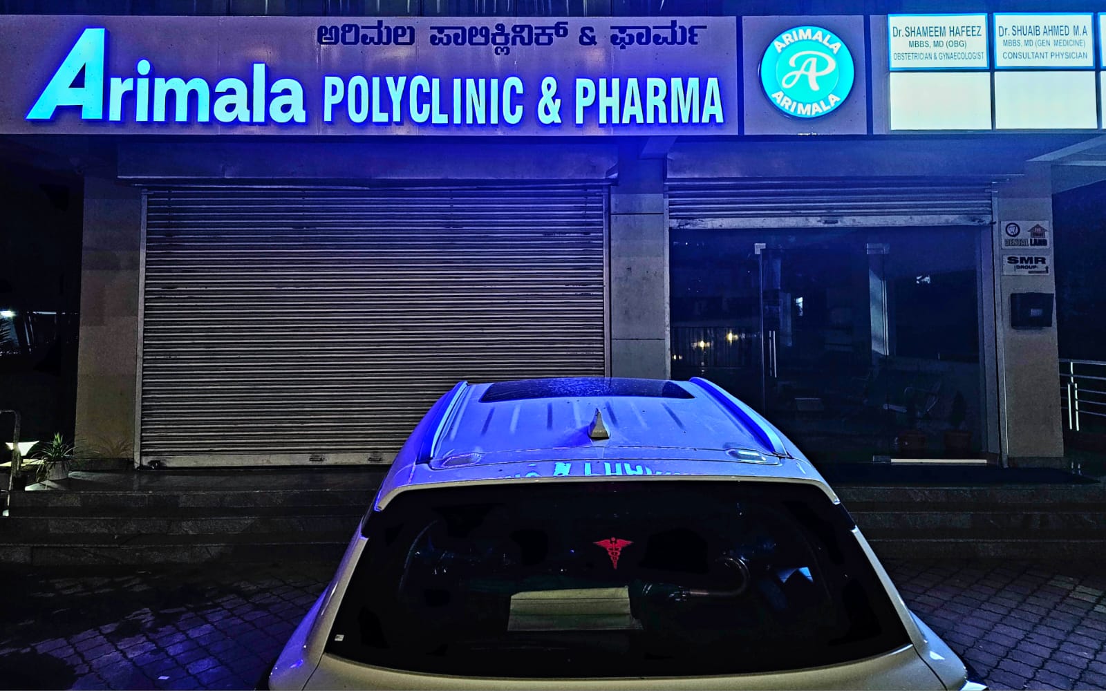 Arimala Polyclinic & Pharma at dusk, its blue signage lit above the entrance on Sturrock Road